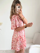 Robe courte corail fleurie Lyséa à manches courtes volantées et taille élastiquée, portée par un mannequin dans un intérieur lumineux.