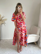 Robe longue imprimé tropical rose fuchsia, corail et bleu avec manches courtes et décolleté cache-cœur.